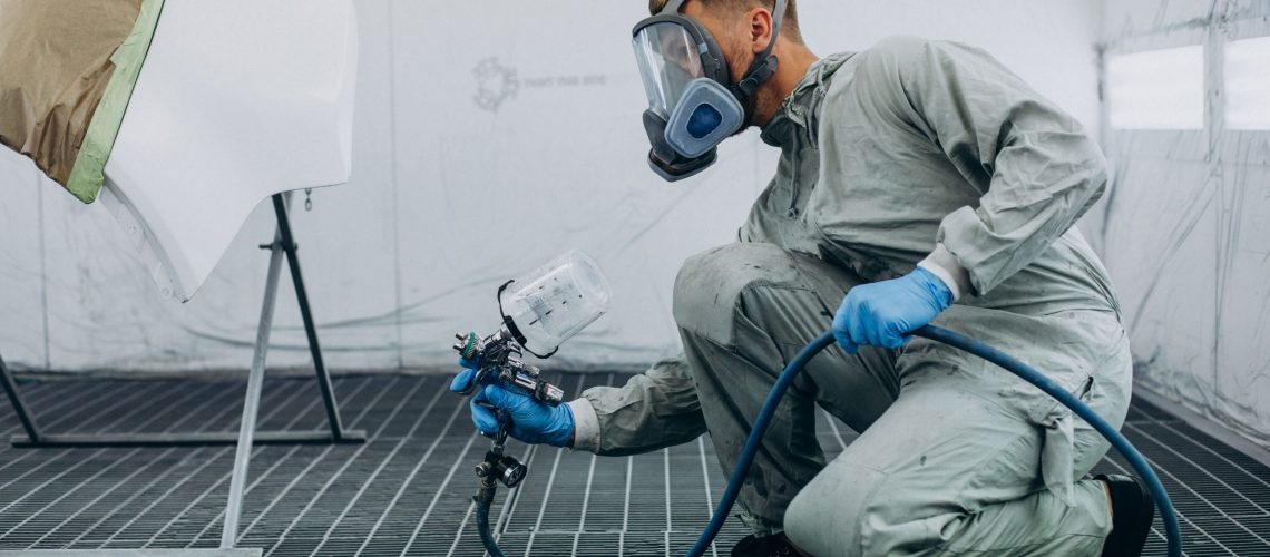 man using industrial paint machine to paint car door white