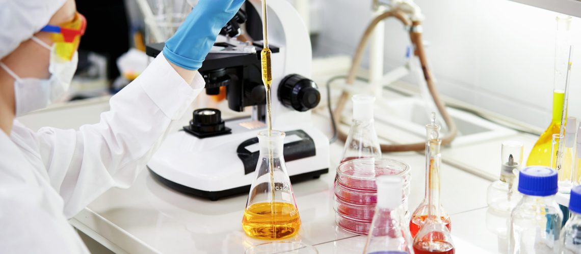 Science, chemistry, technology, biology and people concept - young female scientist mixing reagents from glass flasks and making test or research in clinical laboratory